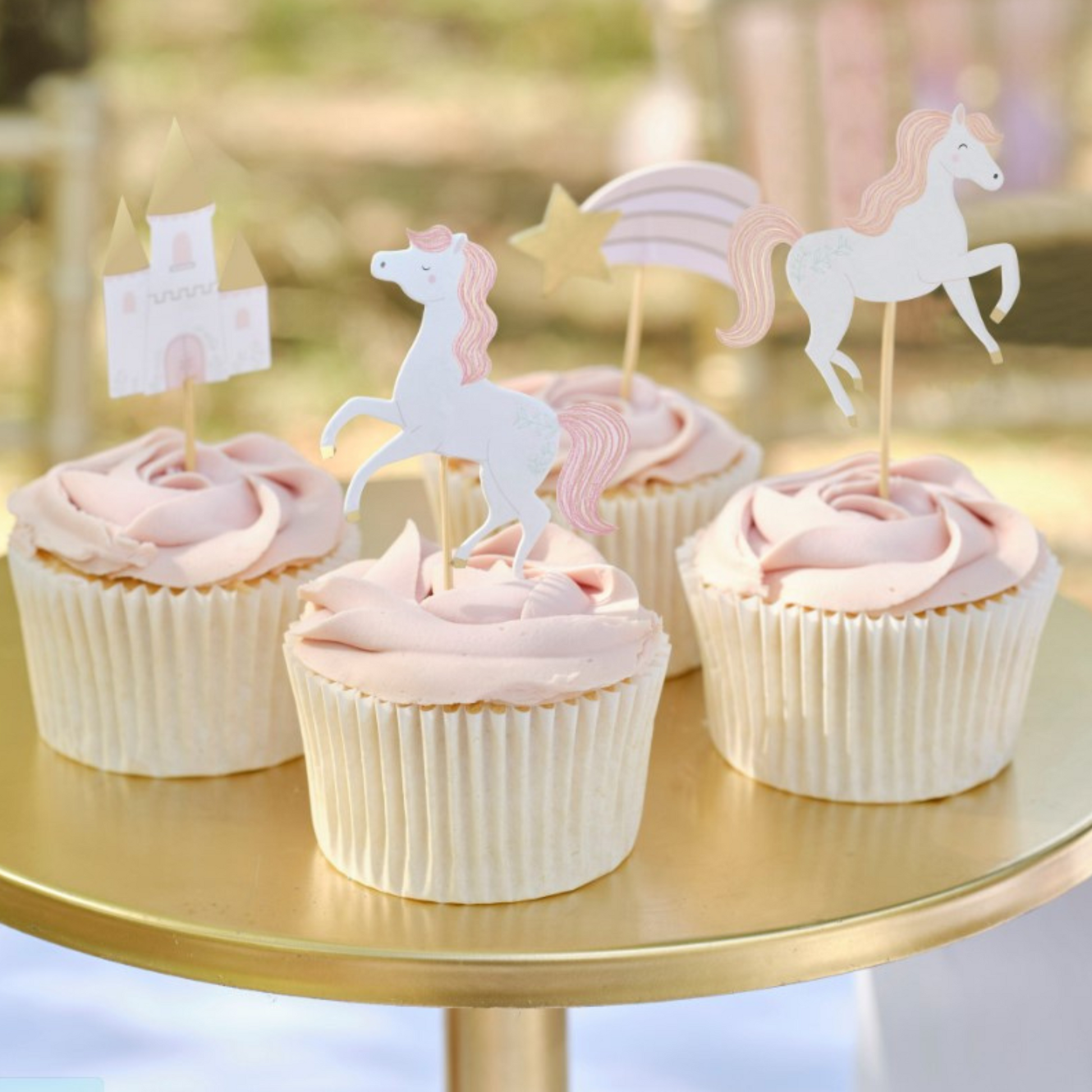 Cupcakes with pink icing and gold cupcake toppers shaped like horses and a castle, designed for a princess-themed party.